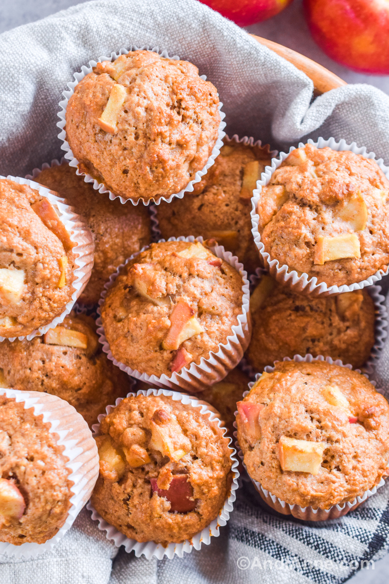 Whole wheat apple muffins piled into a bowl lined with a linen kitchen towel.