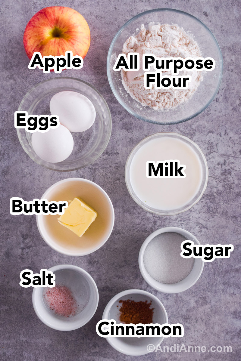 Looking down at recipe ingredients including an apple, and bowls with flour, eggs, milk, sugar, butter, salt and cinnamon.
