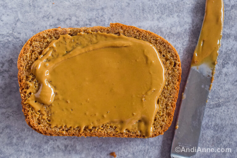A slice of bread with peanut butter spread on top and a knife beside.