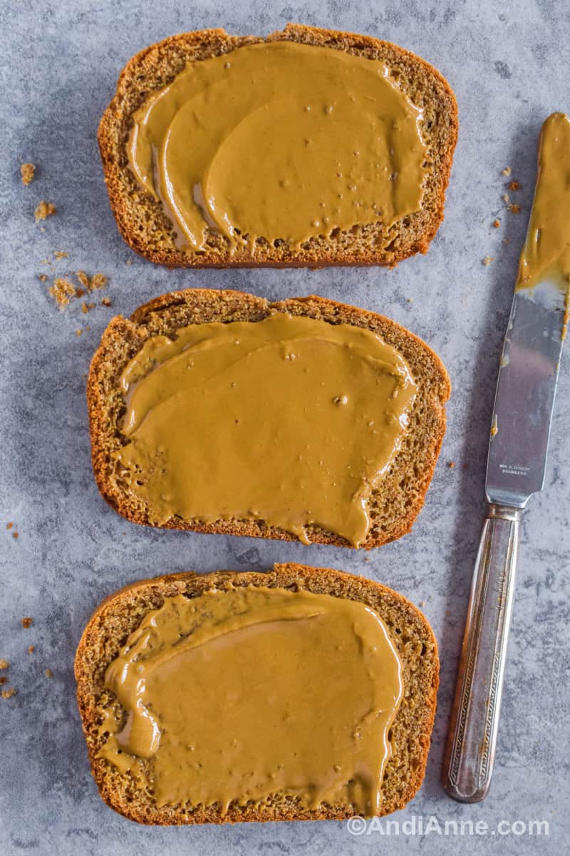 Three slices of bread with peanut butter spread overtop and a butter knife beside it.