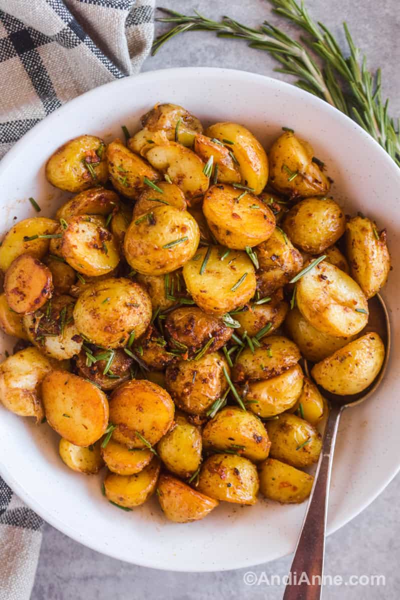 Crispy baby potato slices with chopped rosemary in a white bowl with a spoon.