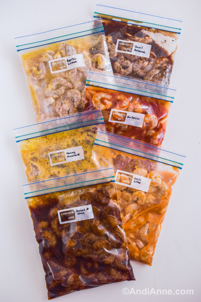 Six ziploc bags with marinated shrimp in various colors of sauces. All piled on a table.