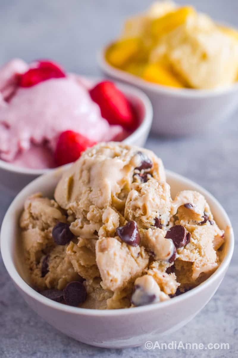 Close up of peanut butter chocolate chip ice cream in a white bowl with strawberry and mango in the background.
