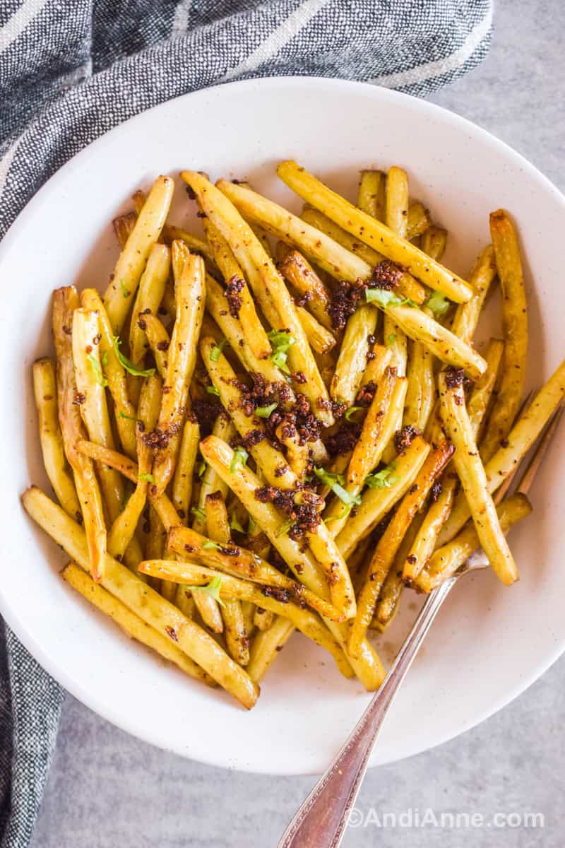 Cooked yellow beans in a white bowl with crispy edges and crispy cooked garlic dumped on top. A fork is on the side in the bowl.
