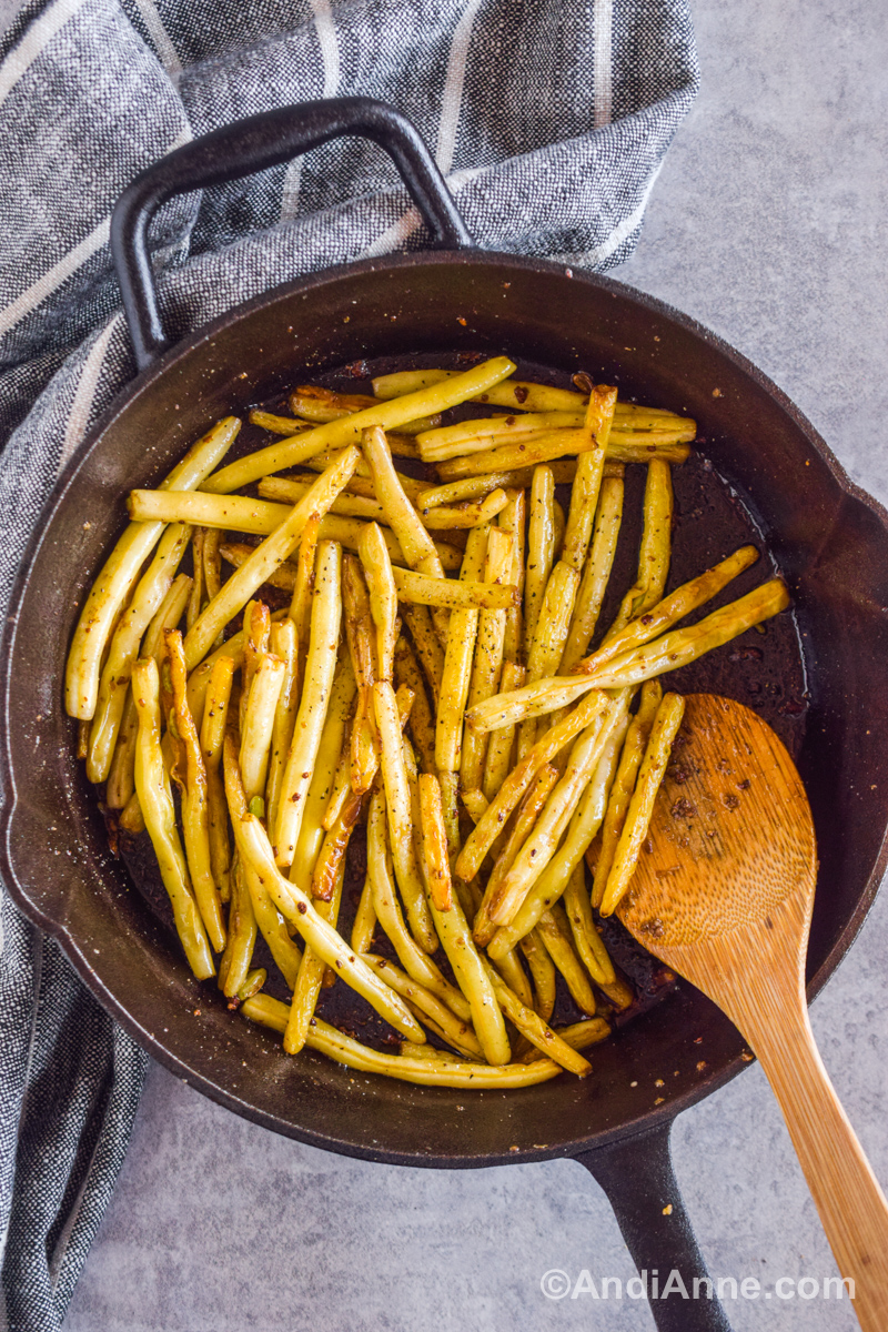 Cooked yellow beans in a black skillet with a wood spoon.