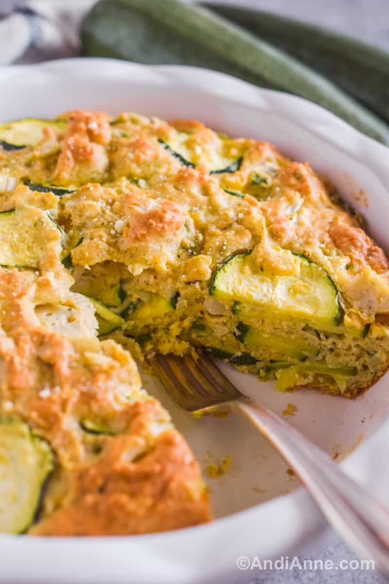 Close up of a fork inside the pie plate with a slice taken out of the zucchini pie so you can see the layers of zucchini slices inside the baked dough.