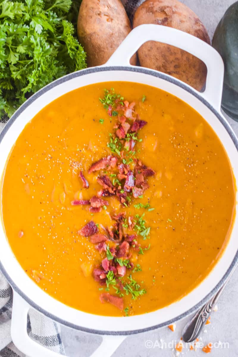 A large white pot with bacon squash soup. Chopped bacon and parsley sprinkled on top.