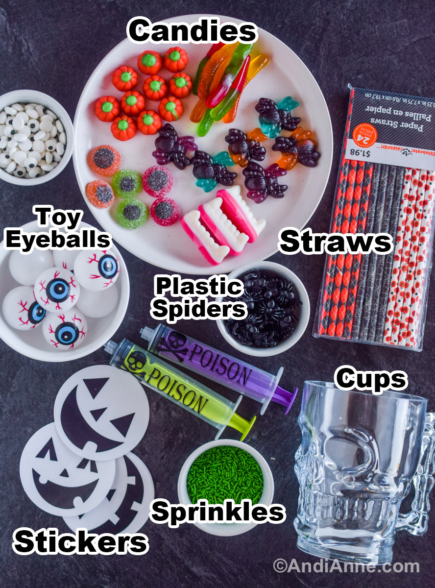 Various props including a plate with different halloween candies, a bag of paper straws, a bowl of toy eyeballs, a plastic skull cup, a bowl of green sprinkles, toy syringes and pumpkin face stickers.