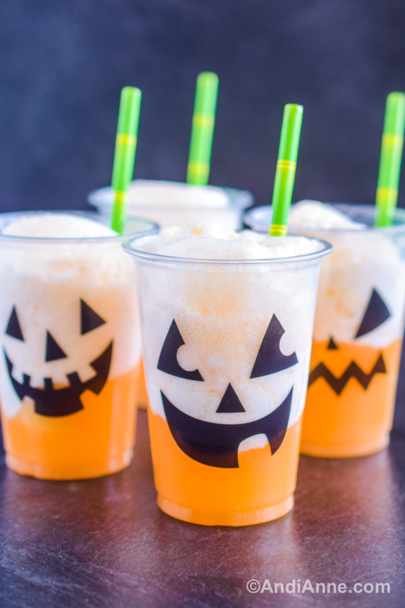 Four jack-o-lantern drinks in plastic cup with black faces on the front and green paper straws.