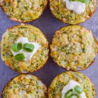 Six zucchini parmesan bites. Some with a dollop of mayo and a few chopped green onions on top.