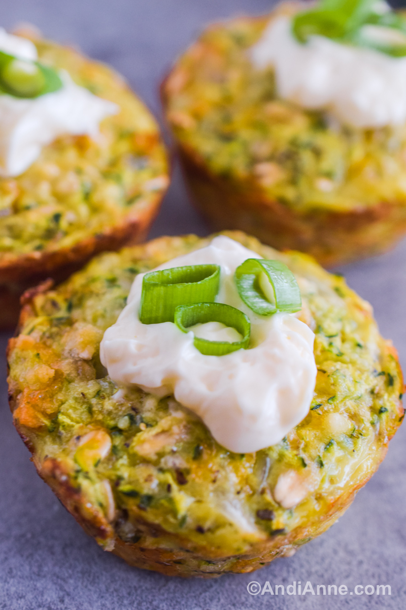 A close up of a zucchini muffin bite with sour cream and green onion on top.
