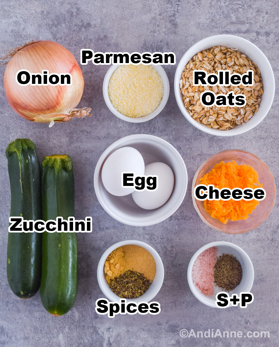 Recipe ingredients on the counter including a yellow onion, bowls of parmesan, rolled oats, cheese, spices and two zucchinis.