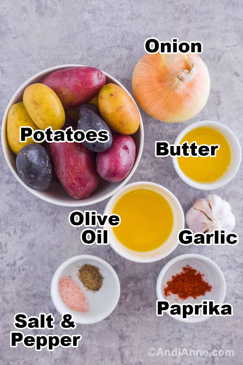 Recipe ingredients on the counter including a bowl of potatoes, an onion, a garlic bulb, and small bowls of butter, olive oil, paprika, salt and pepper.