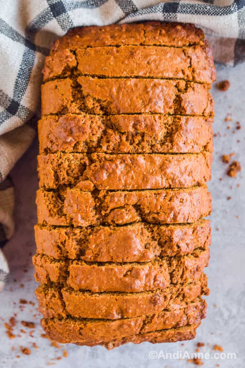 Looking down at brown bread cut into slices but still together in loaf shape with kitchen towel beside it.