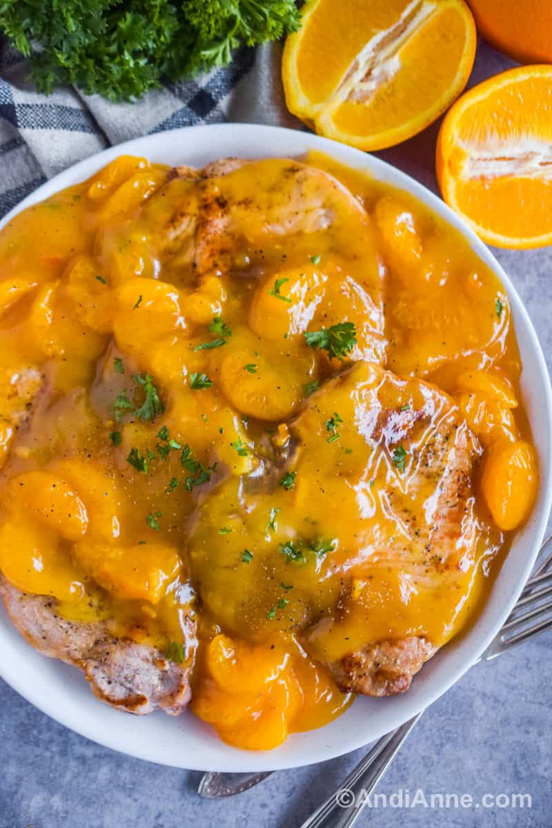 Pork chops on a plate covered in orange sauce with sliced mandarin oranges.