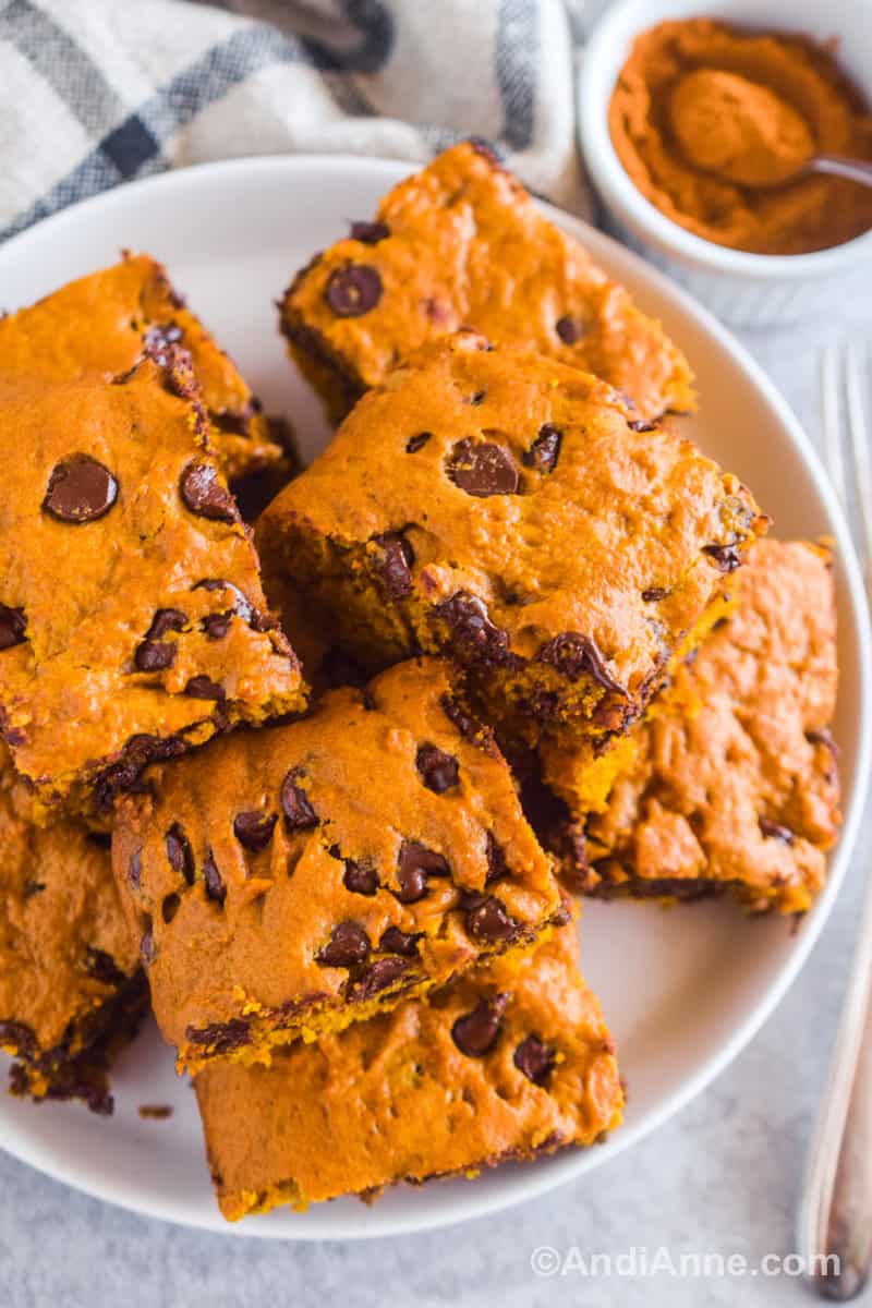 Chocolate chip pumpkin squares piled on top of each other on a white plate.
