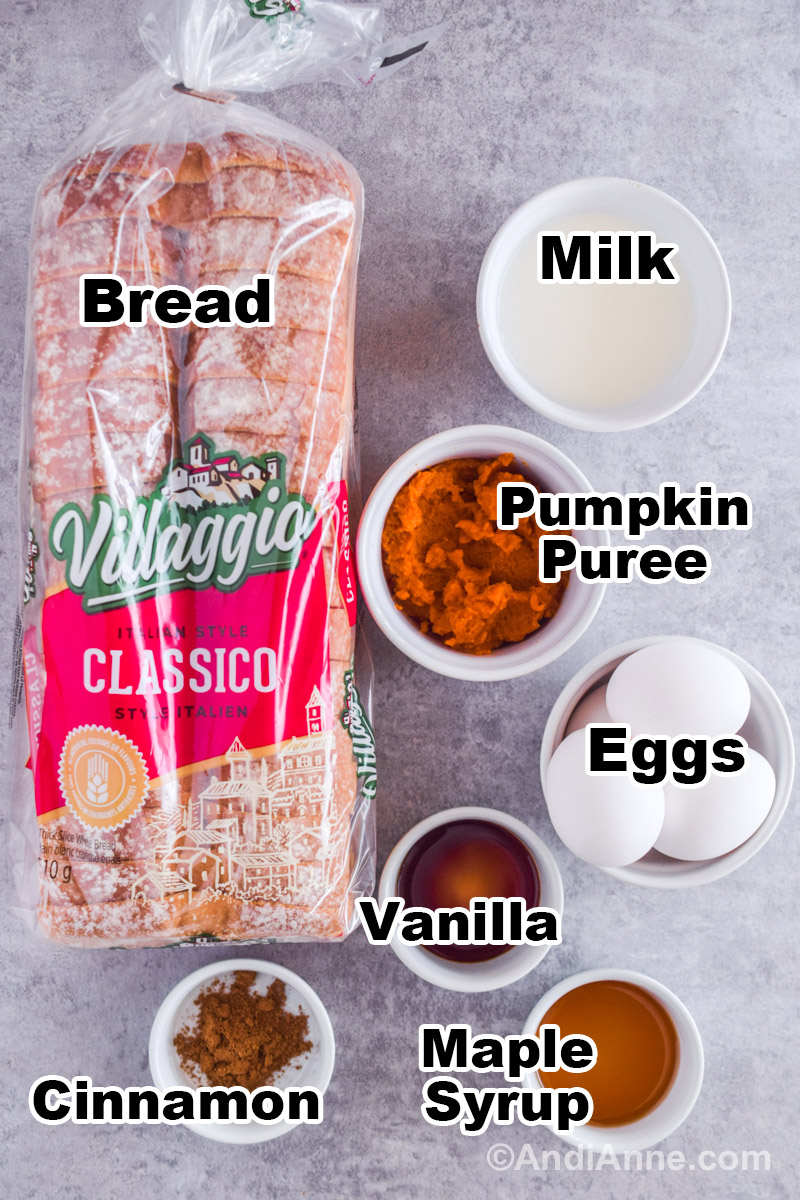 Recipe ingredients on the counter including a loaf of bread, bowl of milk, pumpkin puree, eggs, vanilla, cinnamon and maple syrup.