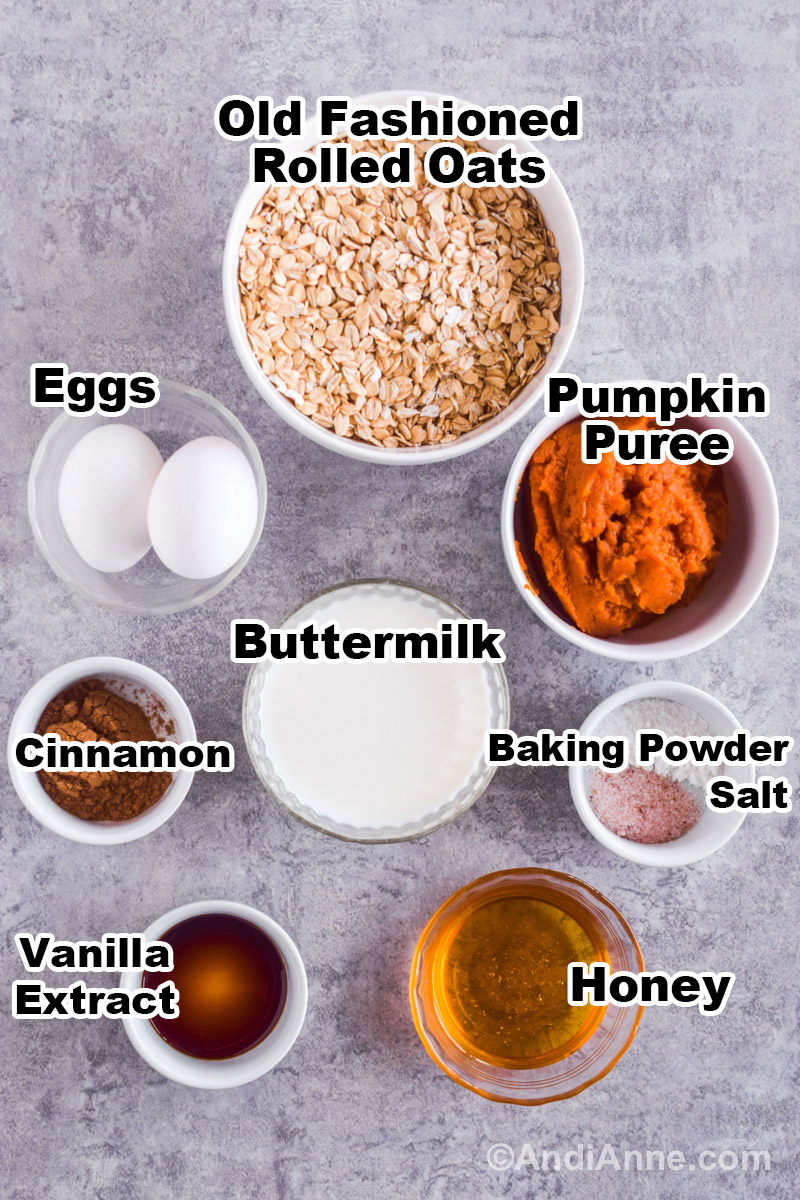 Recipe ingredients on a counter including a white bowl with rolled oats, bowl with pumpkin puree, eggs, buttermilk, cinnamon, honey, vanilla, baking powder and salt.