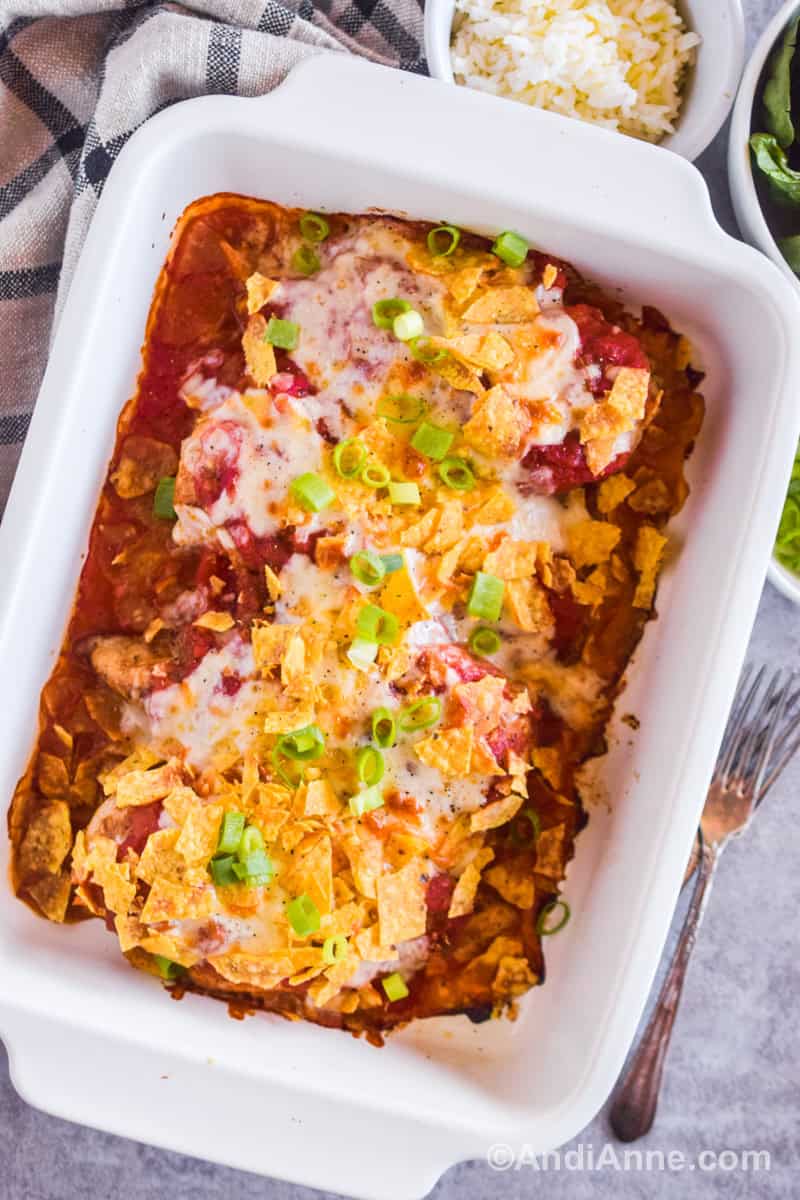 A baking dish with salsa mozzarella chicken breasts with forks and bowls of small ingredients beside it.