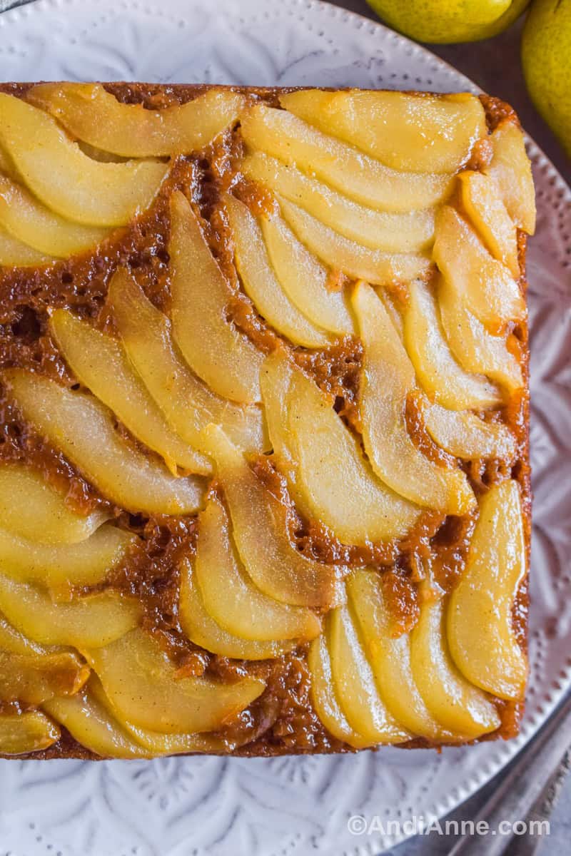 Looking down at the sliced pears on a brown square cake, sitting on a white decorative plate.