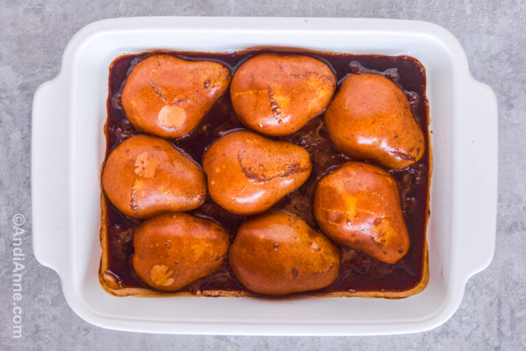 Pears sliced in half in a brown sauce in casserole dish.
