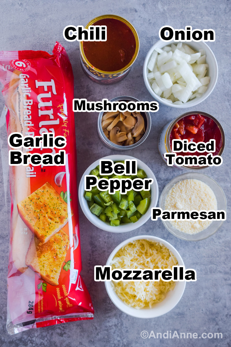 Ingredients to make the recipe including a bag with garlic bread inside, bowls of chopped onion, chopped bell pepper, grated parmesan, shredded mozzarella, canned chili, canned mushrooms and canned diced tomatoes.