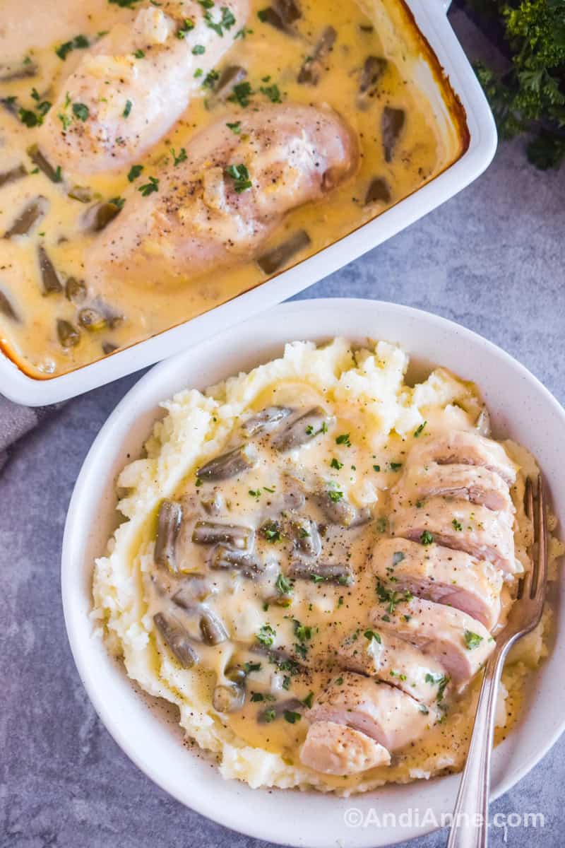A white plate with mashed potatoes, sliced chicken breast, green beans and a fork. Baking dish with more of the recipe is beside it.