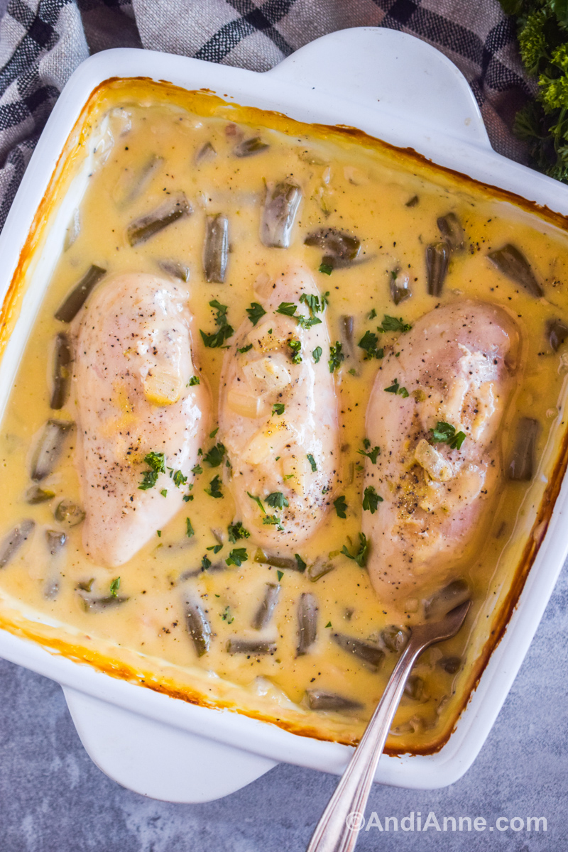 A white dish with cream of chicken soup sauce, green beans and chicken breasts.