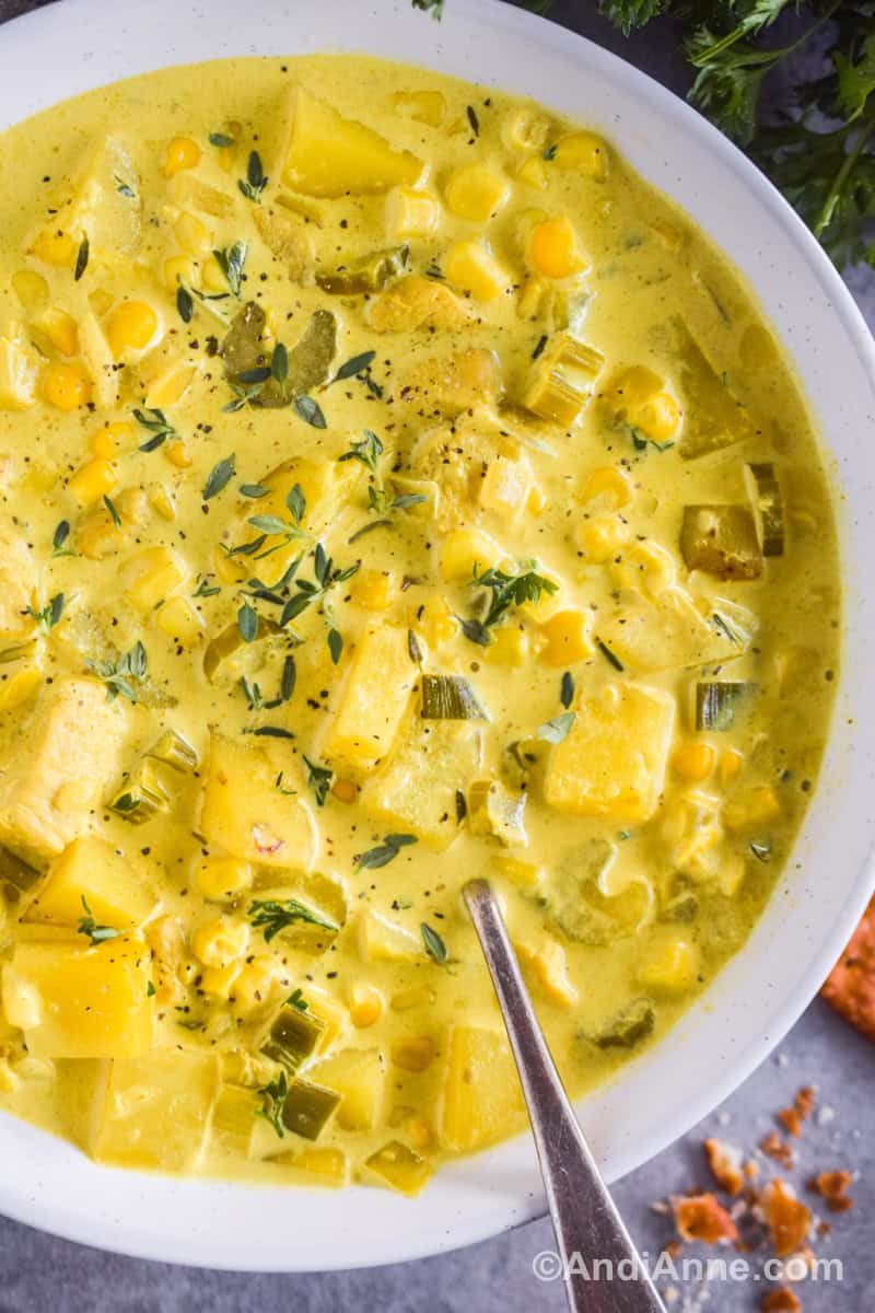 Close up of a white bowl of curry corn chicken chowder with a spoon.