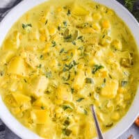 A bowl of curry chicken corn chowder with a spoon.