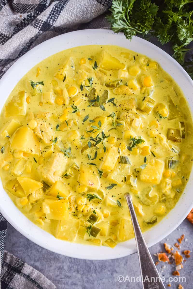 Close up of a bowl of yellow soup with chopped potatoes, chicken, celery and corn.