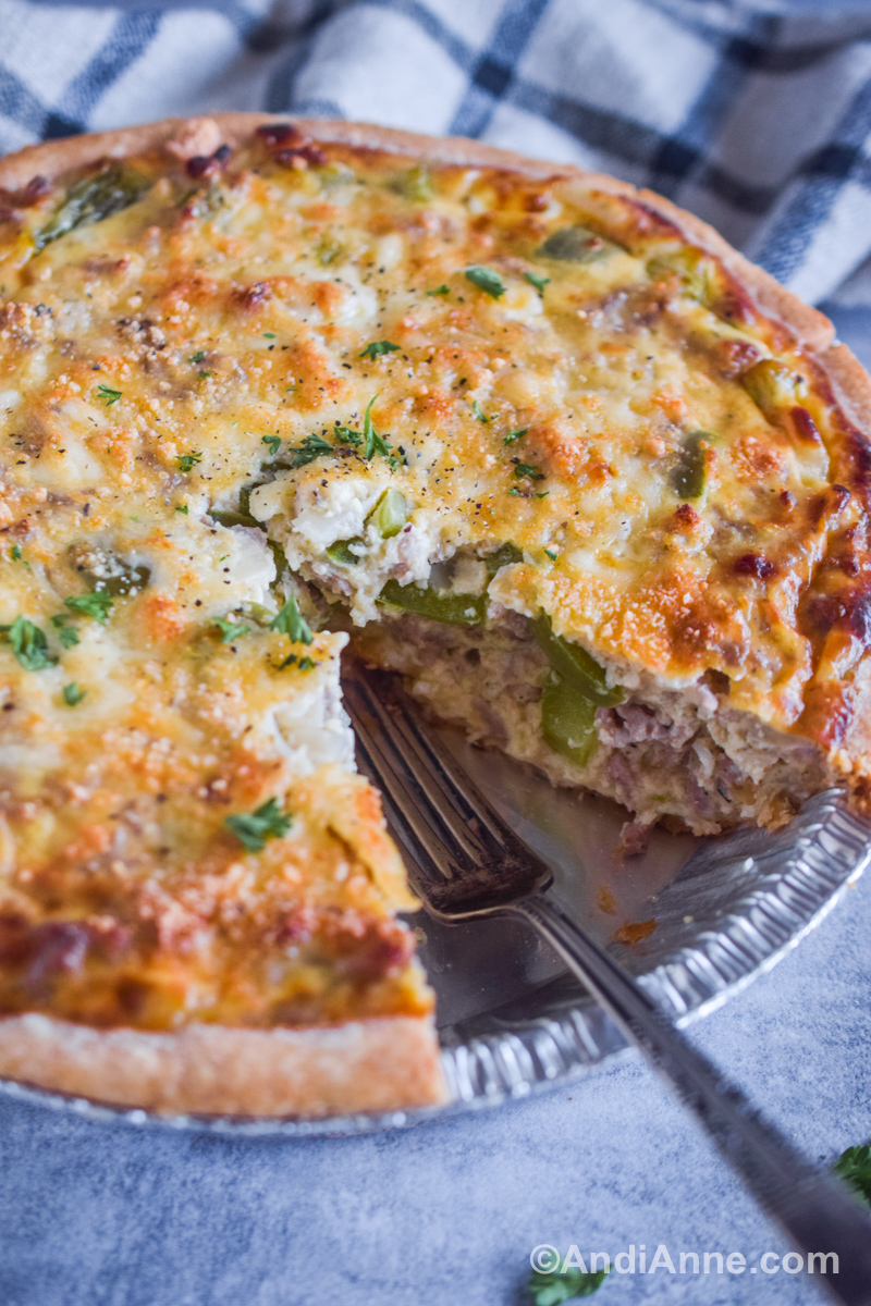 Close up of the full quiche with a slice taken out and a fork in its place.