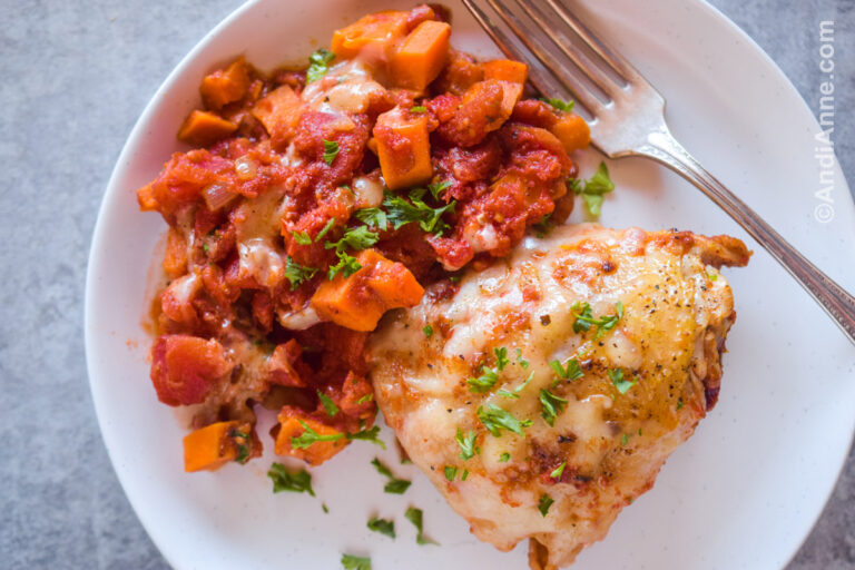 A white plate with one cooked chicken thigh and chopped sweet potato and diced tomatoes.