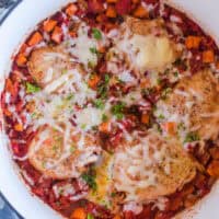 A white pot with chicken, tomatoes and sweet potatoes. Topped with melted mozzarella cheese.
