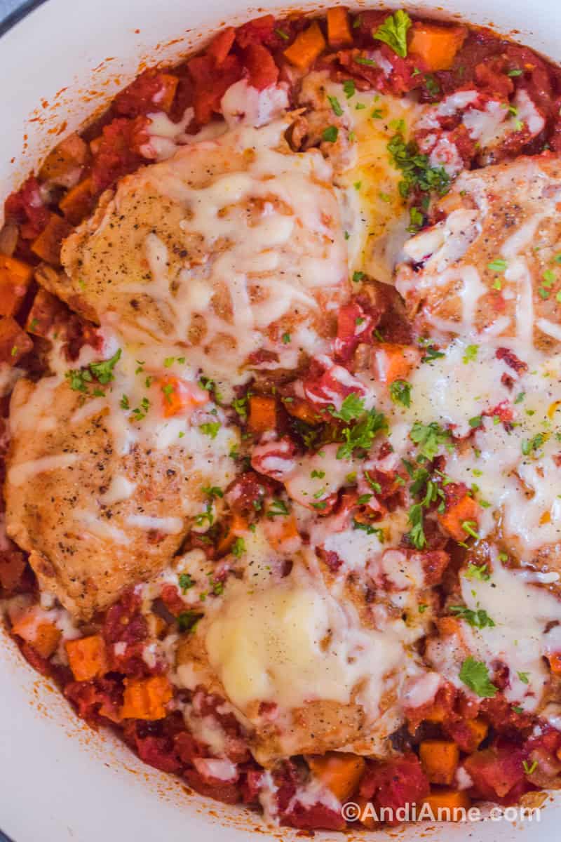 Close up of melted cheese on top of cooked chicken thighs, diced tomatoes and chopped sweet potatoes.