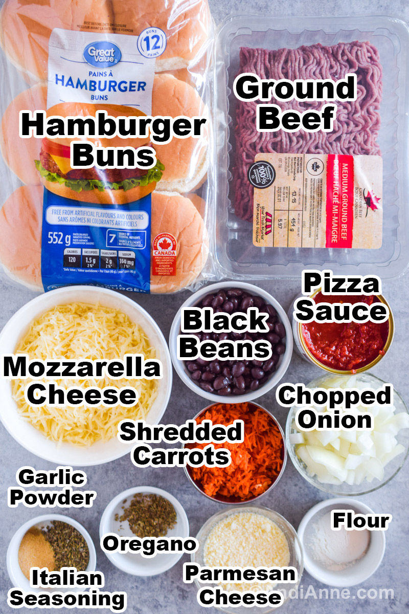Recipe ingredients on the counter including a bag of hamburger buns, raw ground beef, bowls of cheese, black beans, pizza sauce, shredded carrots, flour and spices.