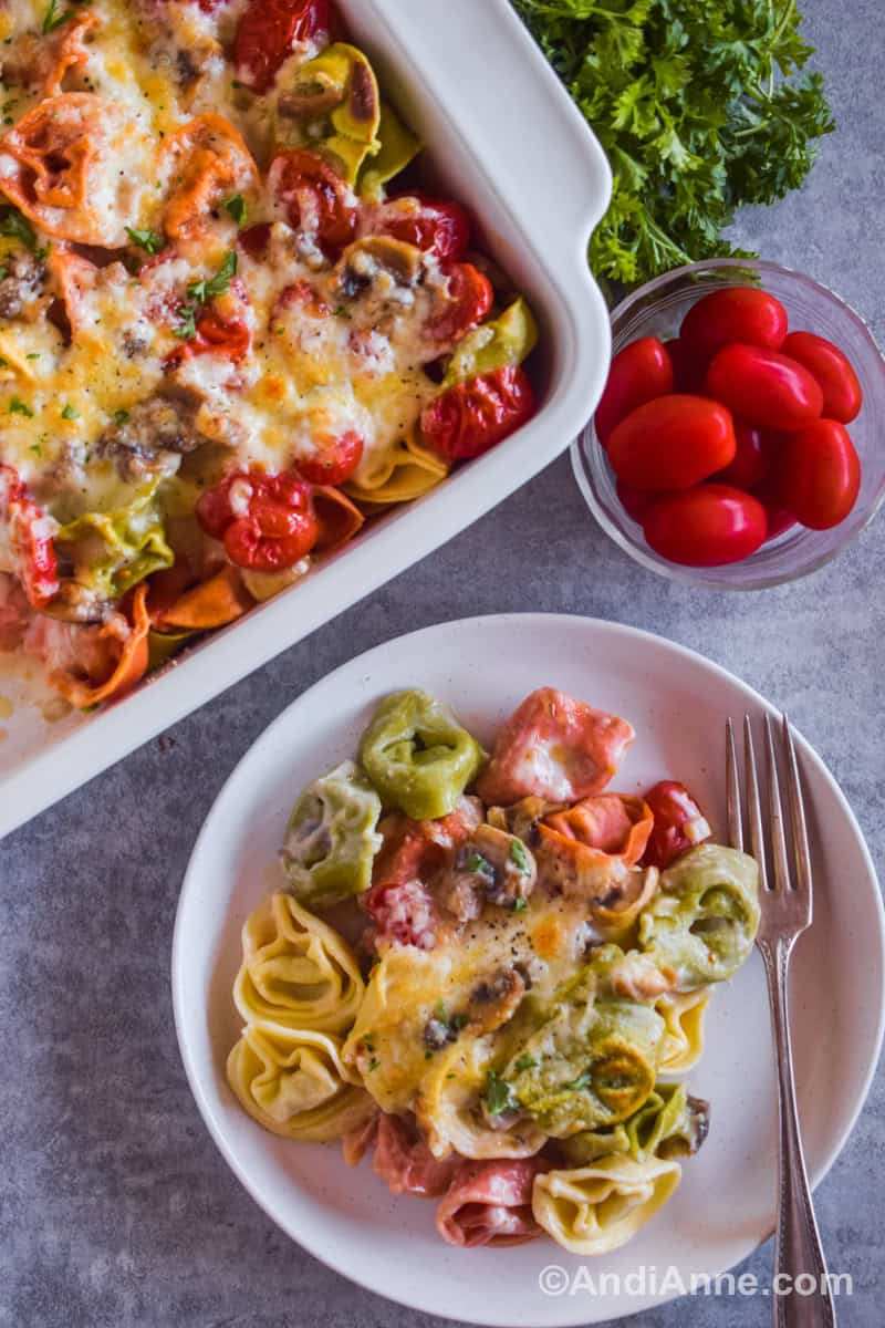 A plate with tortellini pasta, mushrooms and cheese and a fork. The casserole dish is beside it.